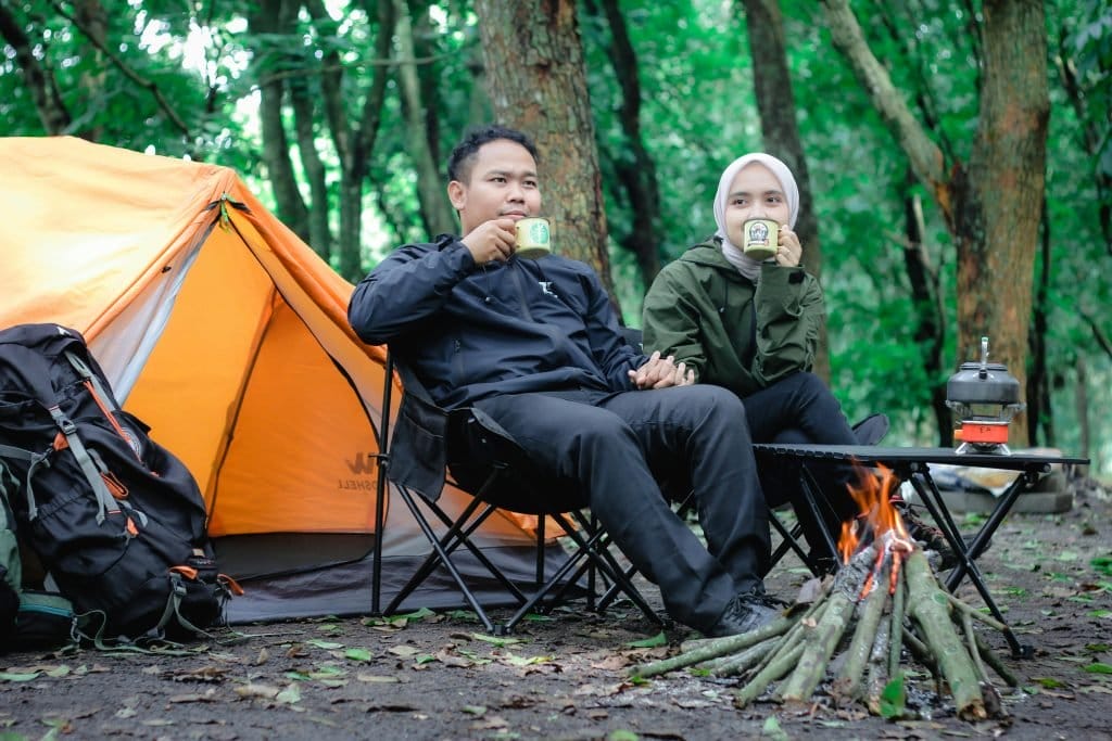 couple drinking coffee in front of tent in forest