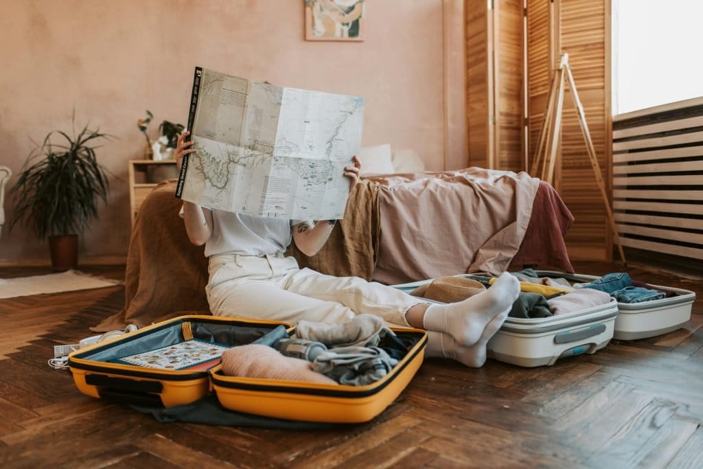 person looking at map on the floor near the bed with two open suitcases