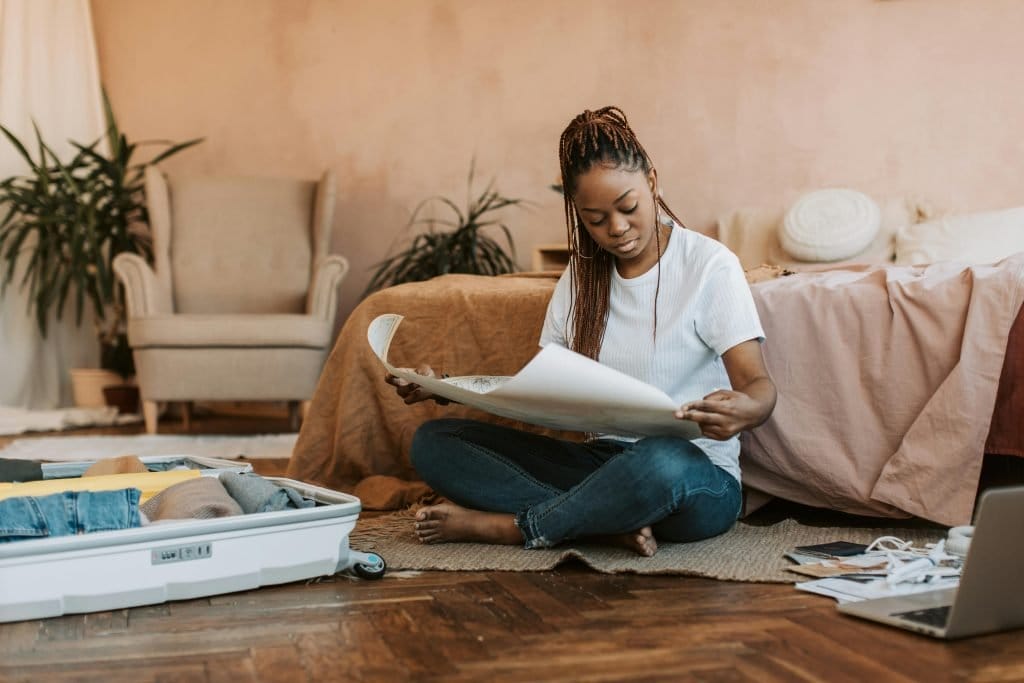 black woman on floor in bedroom packing and looking a map